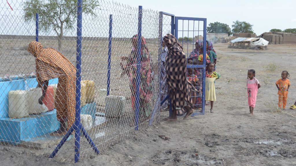 Women and children collecting safe drinking water from a newly constructed water pump in White Nile State – Photo courtesy of Sudan CAFOD